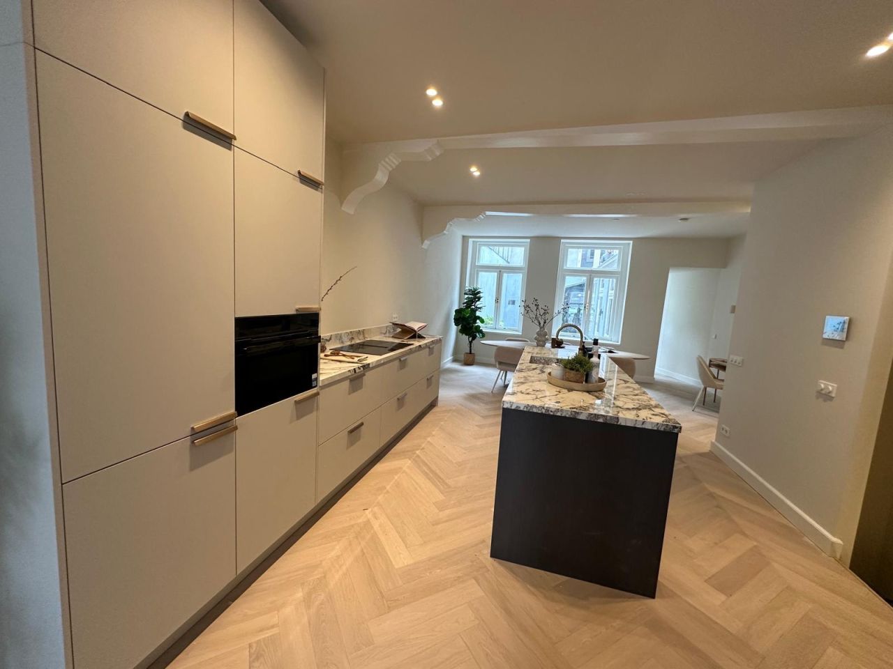 Opgeleverde woonkeuken met marmeren kookeiland en visgraatvloer na complete woningrenovatie