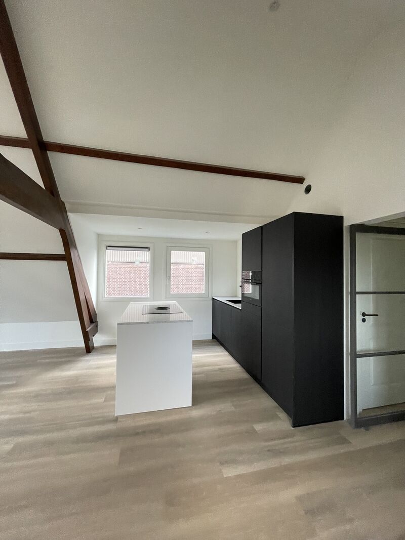 Keuken onder de kap met zwarte kasten en houten spanten na een verbouwing