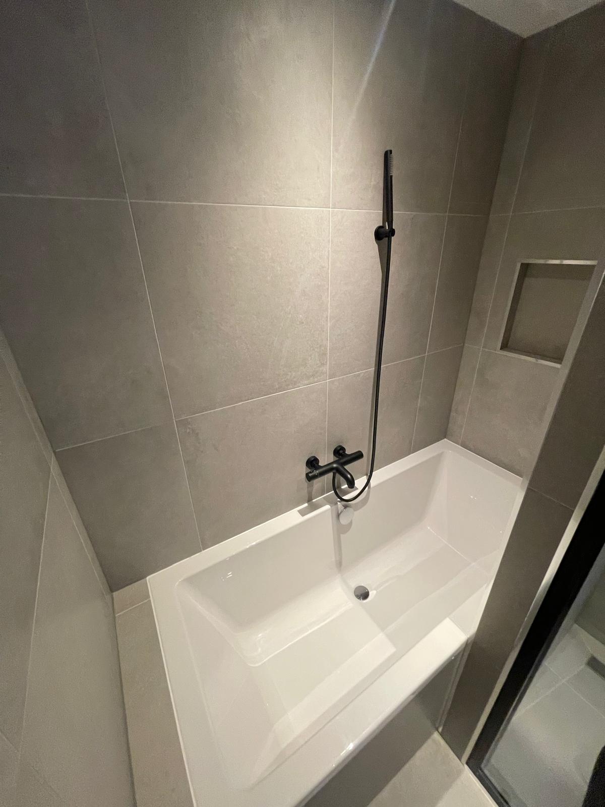 Nieuwe badkamer met ligbad en grote tegels in een gerenoveerde portiekflat in de Tarwewijk in Rotterdam-Zuid