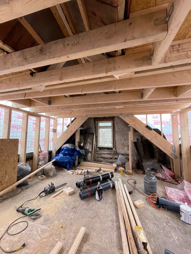 Woning tot op de constructie gestript: blootliggende houten kapconstructie en dakbeschot tijdens een cascorenovatie